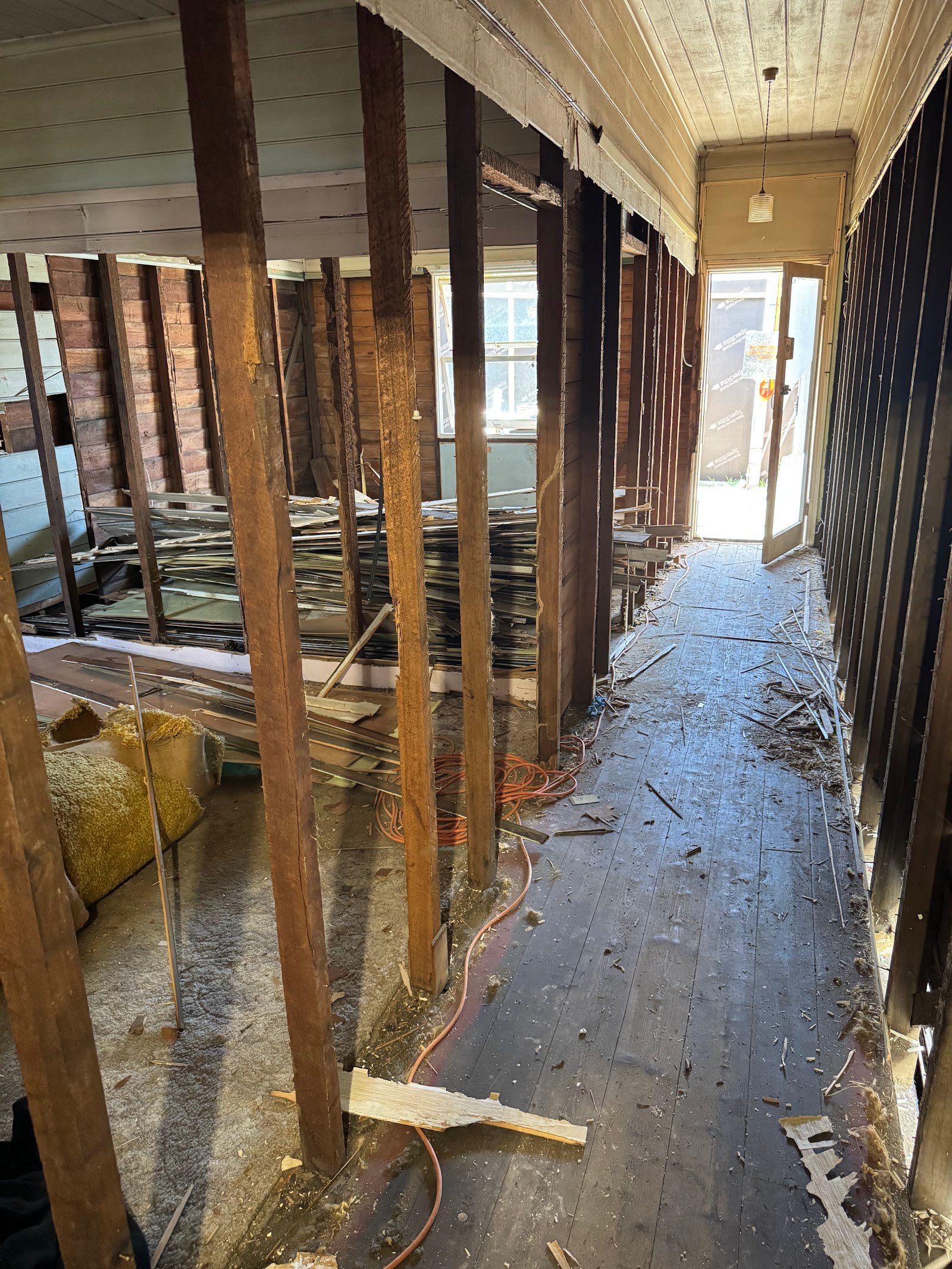 Interior demolition of the Clovelly cottage with walls stripped to timber studs, Black Willow Group